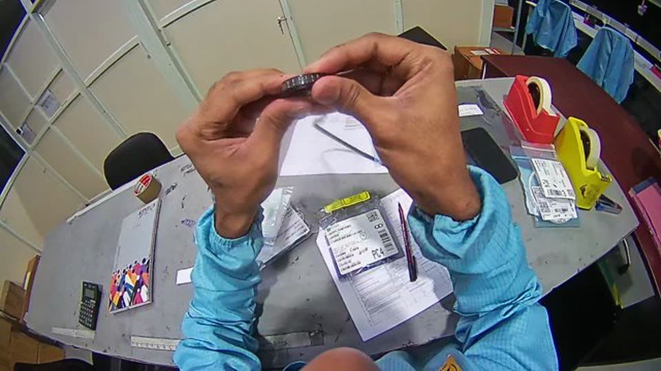 A worker at an electronics workbench handling packaged components
